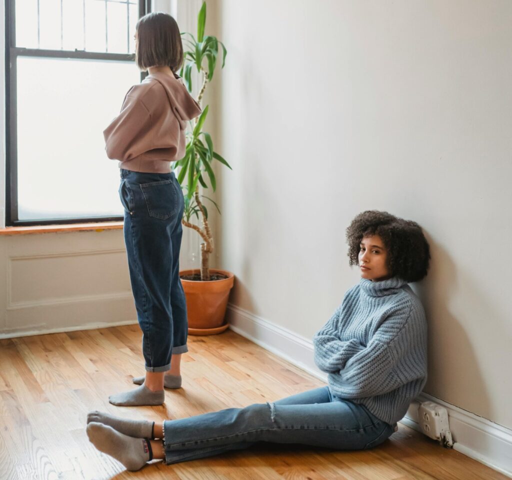 Two women in a room, one sitting and one standing, showing signs of conflict and tension.